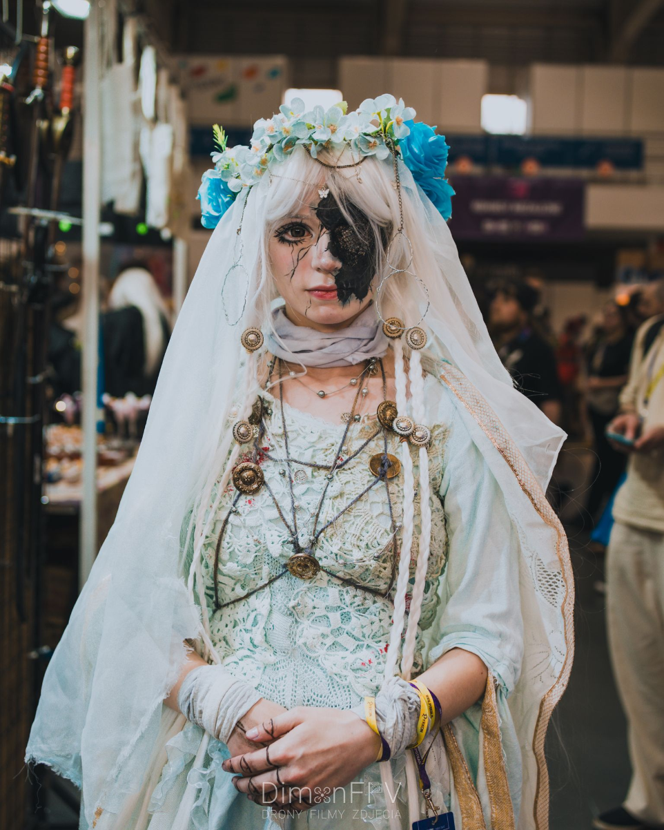 Cosplayerka w stylizacji Elden Ring z koroną z kwiatów, białą peruką i efektownym czarnym makijażem na oku, sfotografowana na konwencie cosplay Pyrkon